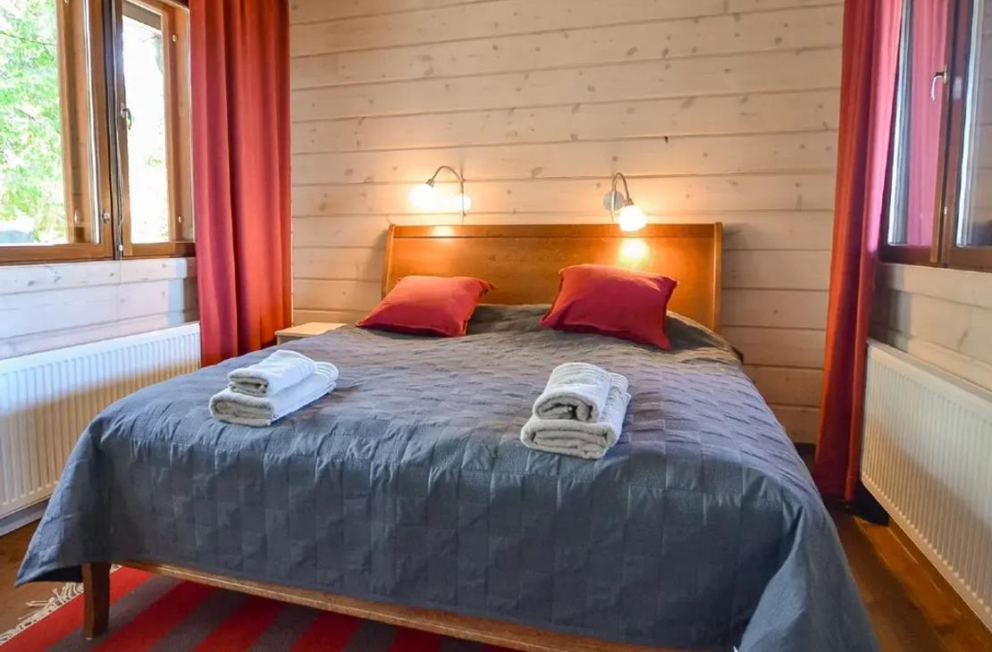 Makuuhuone parivuoteella, punainen tehostev&auml;ri verhoissa ja tyynyiss&auml;