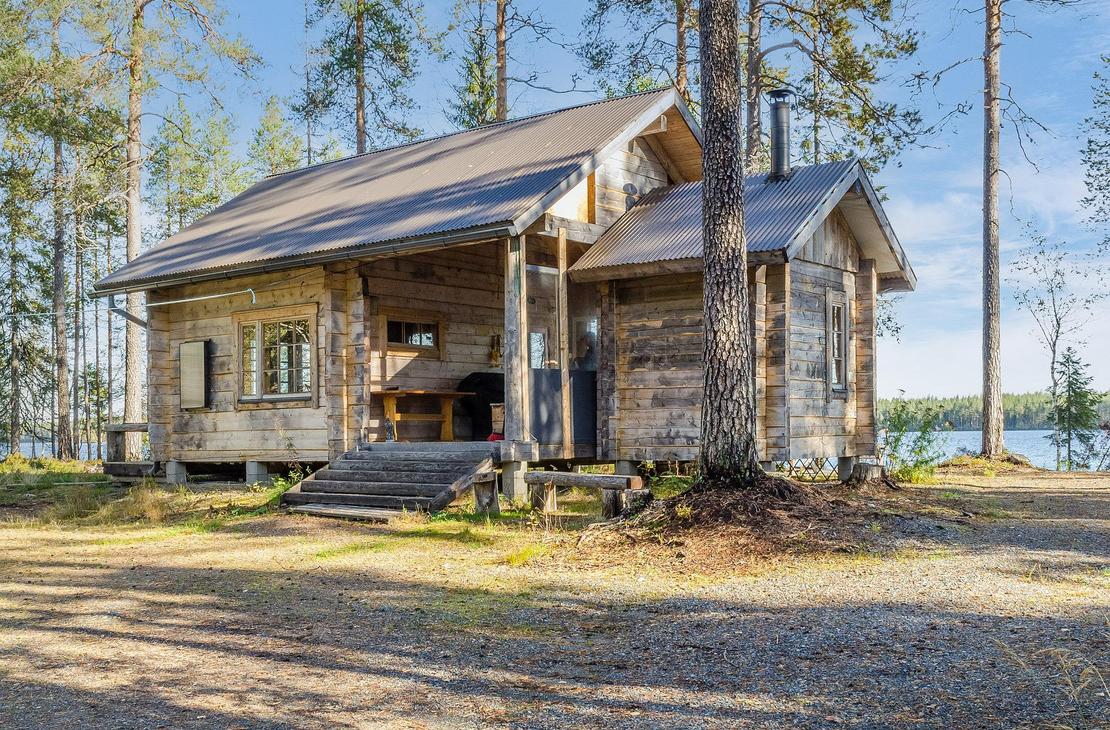 Hirsimökki ulkoa mäntyjen katveessa aurinkoisena päivänä