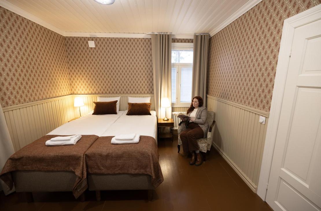 Vaalean ja punaruskean sävyinen huone, jossa kaksi sänkyä ja puiset vaaleat puolipaneelit.