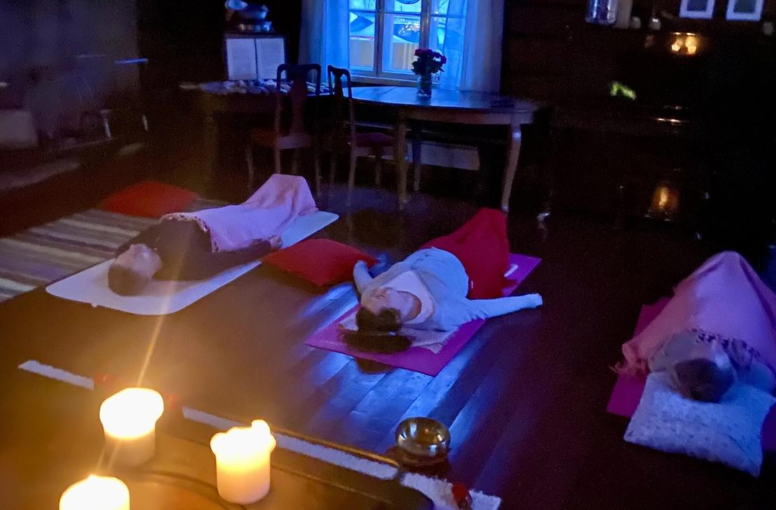 Ihmisi&auml; kuuntelemassa rentoutusta v&auml;rikk&auml;iden vilttien alla h&auml;m&auml;r&auml;ss&auml; kynttil&auml;n valossa