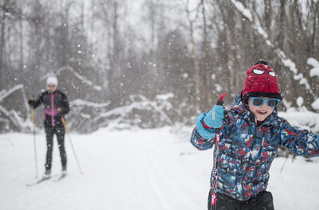 Etualalla innokas nuori hiihtäjä lumisessa metsässä.