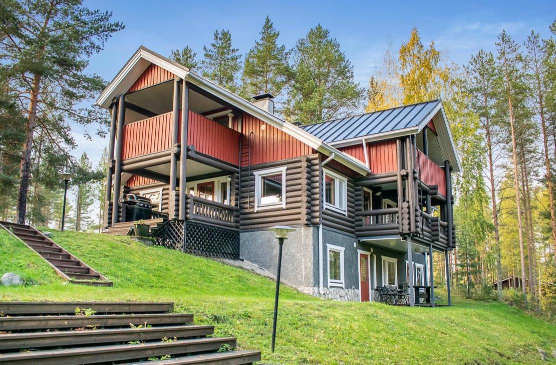 Ruskea-punainen, kolmikerroksinen hirsihuvila nurmirinteessä
