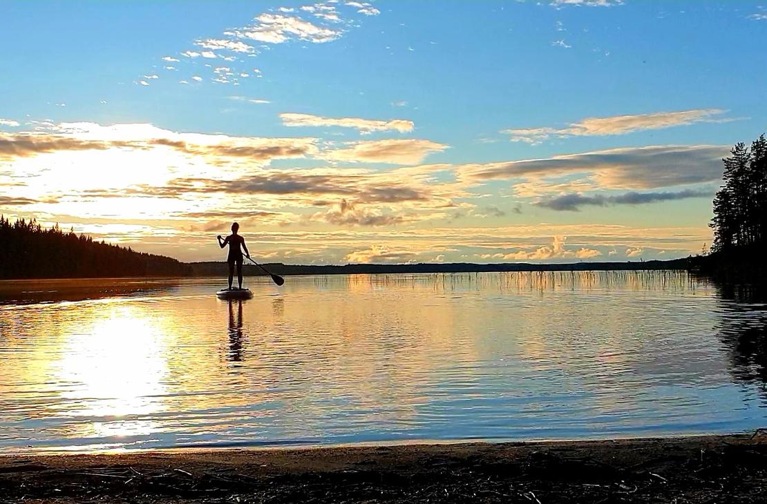 Suppailija tyynell&auml; j&auml;rvell&auml; auringon laskiessa niemen taa