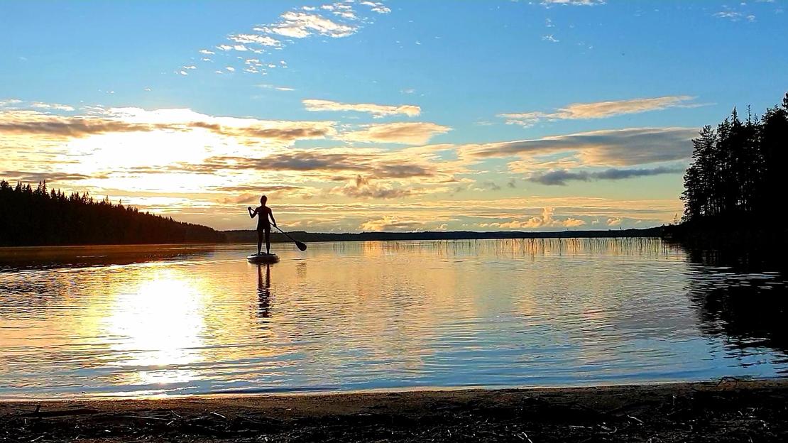 Suppailija tyynellä järvellä auringon laskiessa niemen taa