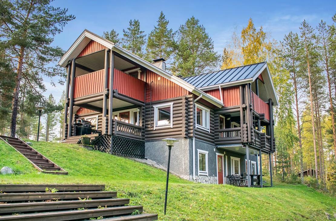 Ruskea-punainen, kolmikerroksinen hirsihuvila nurmirinteessä