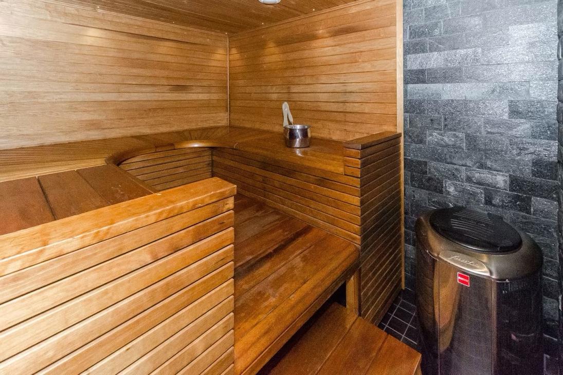 Sauna, jossa harmaa laattaseinä kiukaan takana ja umpinaiset lauteet