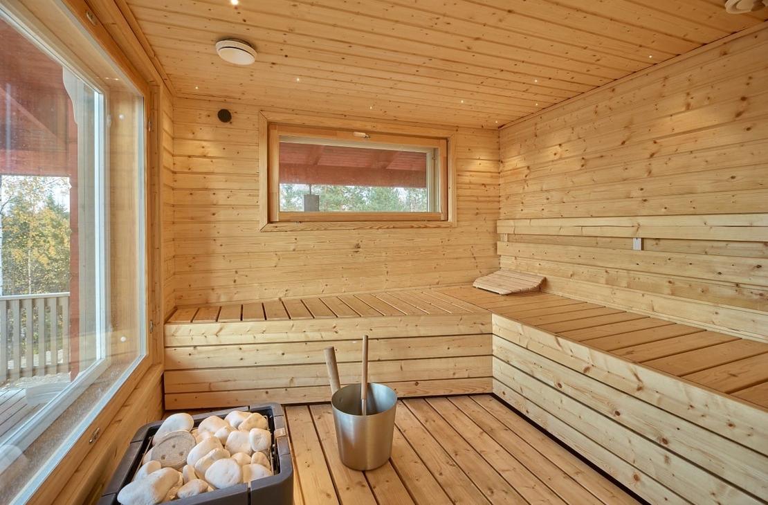 Vaaleaa puuta oleva sauna, leve&auml;t lauteet ja iso maisemaikkuna