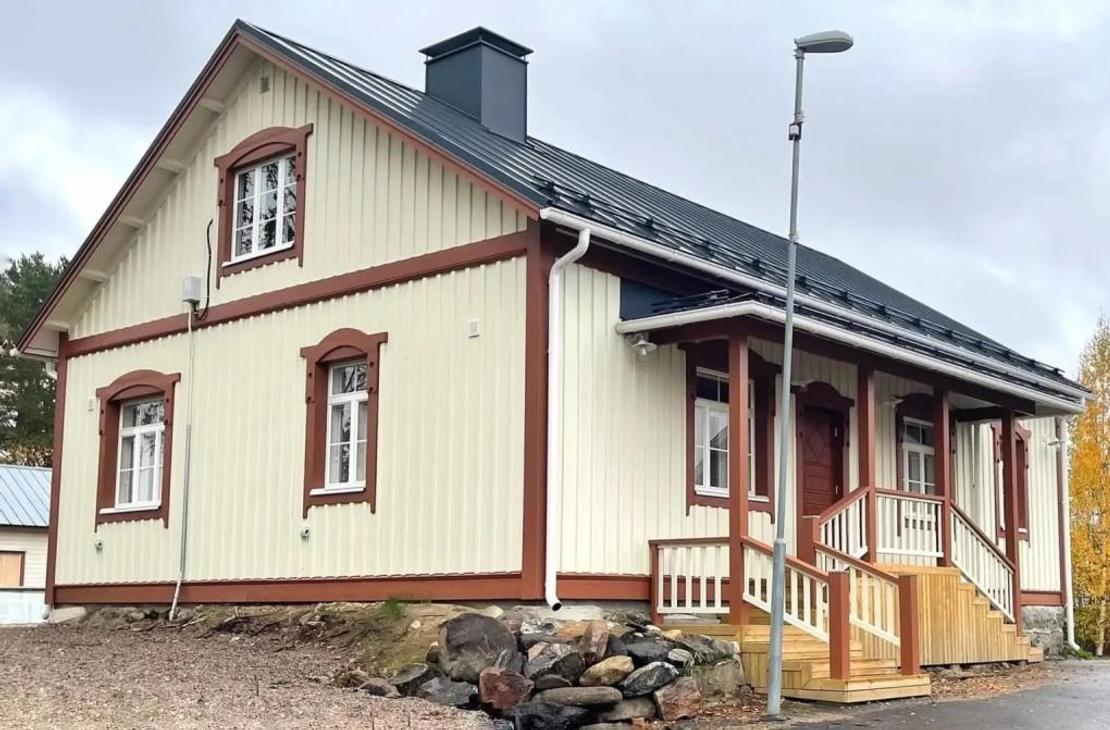 Vaalea kaksikerroksinen puutalo, jossa on viisi huonetta ja ruosteenv&auml;riset koristelaudat.