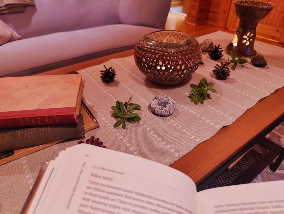 Pöydällä pitsikeraaminen kynttilä, kirjoja ja luonnon koristeita