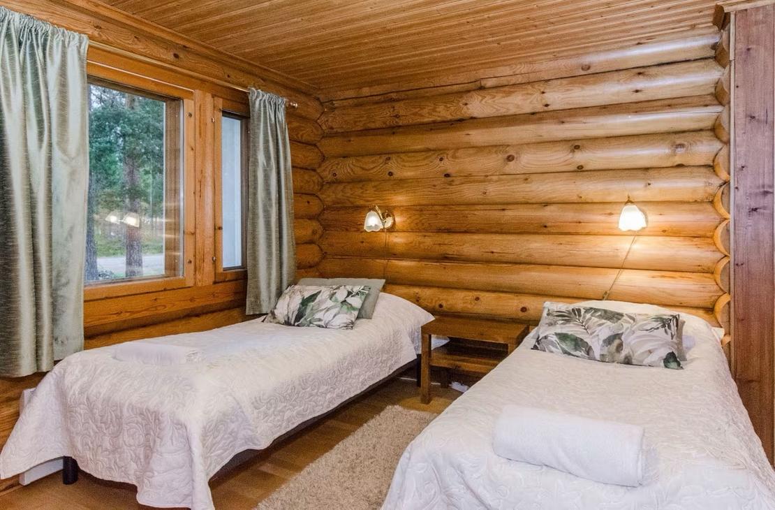 Pyöröhirsiseinäinen makuuhuone, jossa kaksi sänkyä ja vaaleat sänkypeitot