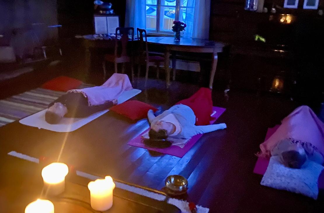 Ihmisiä kuuntelemassa rentoutusta värikkäiden vilttien alla hämärässä kynttilän valossa