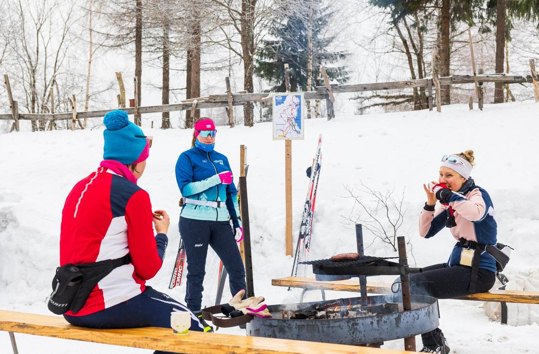 Kolme hiihtäjää evästauolla nuotion ympärillä