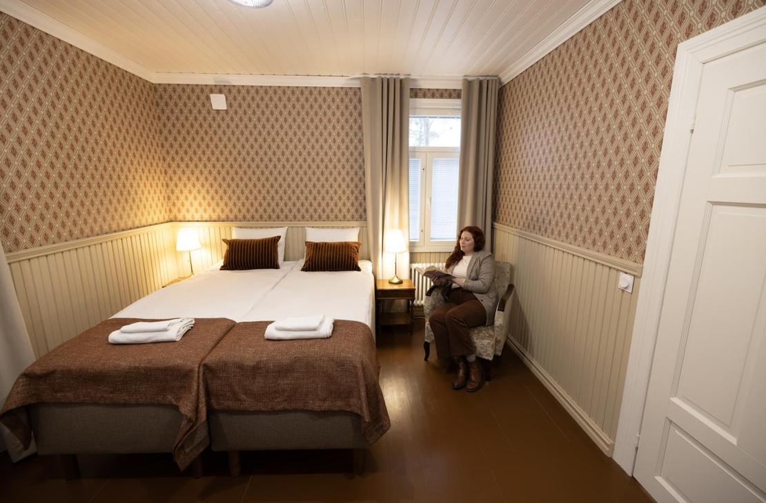 Vaalean ja punaruskean sävyinen huone, jossa kaksi sänkyä ja puiset vaaleat puolipaneelit.