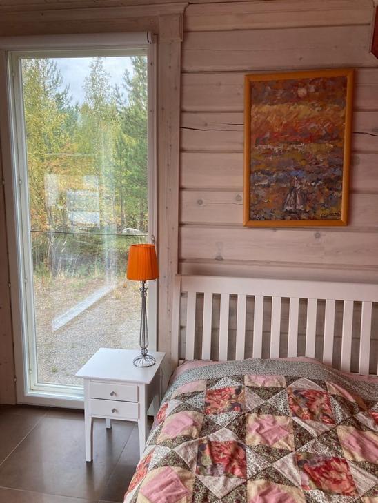 Vaaleanpuna-vihreä-valkoinen tilkkupeitto sängyllä, vierellä maisemaikkuna