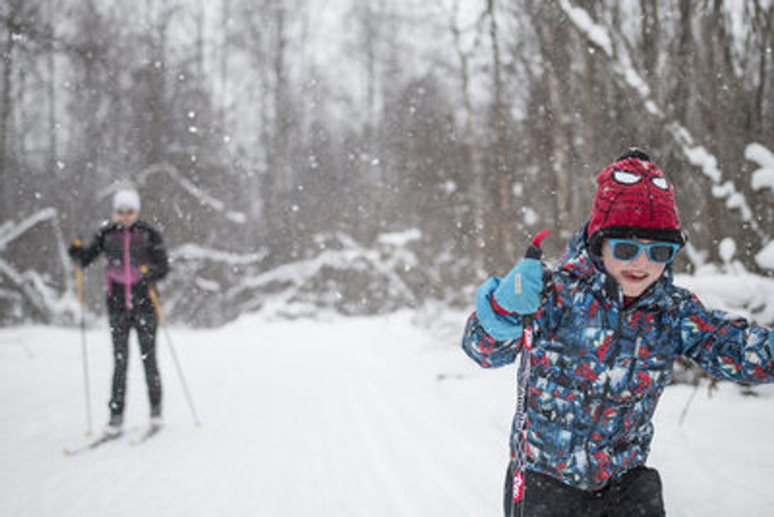 Etualalla innokas nuori hiihtäjä lumisessa metsässä.