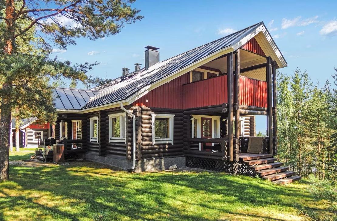 Ruskea-punainen, kolmikerroksinen hirsihuvila mäntyjen katveessa