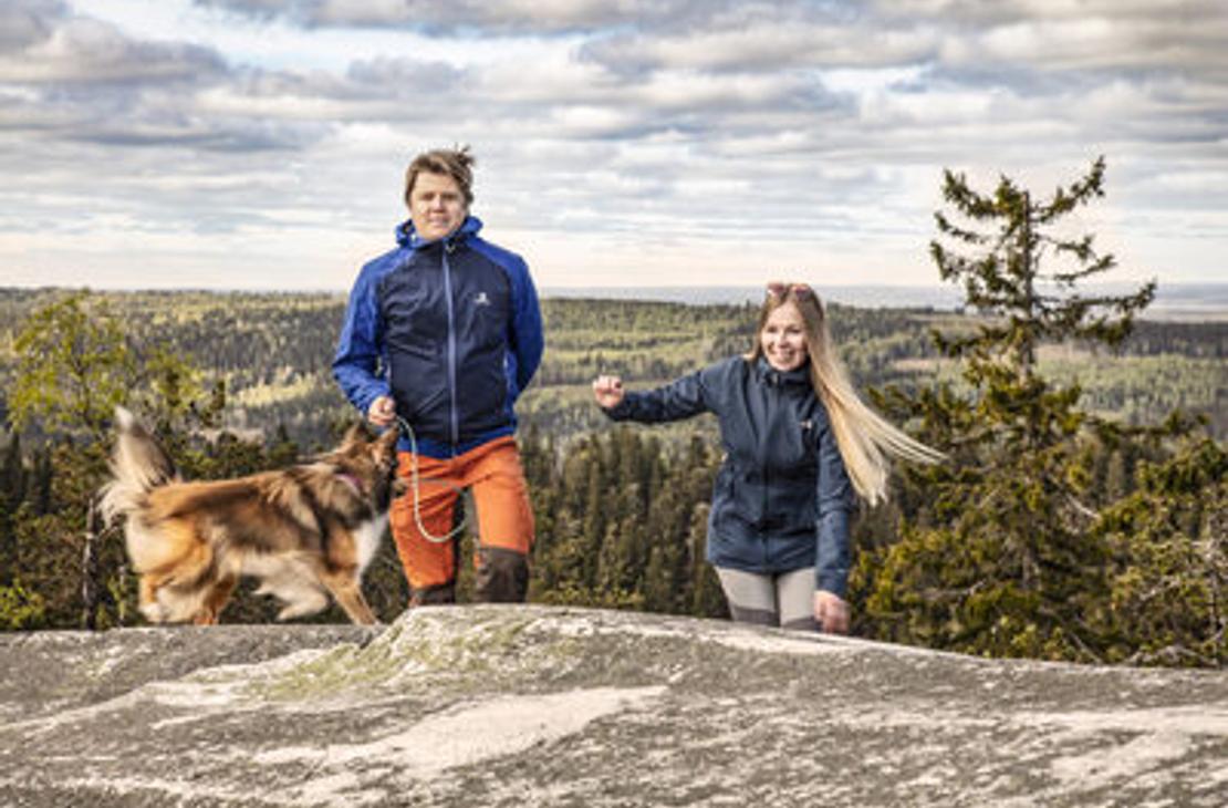 Kaksi retkelijää ja koira nousemassa kalliolle Kolin huipulla