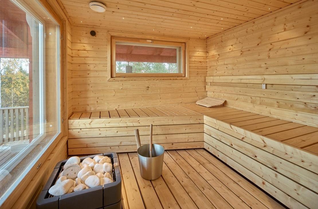 Vaaleaa puuta oleva sauna, leve&auml;t lauteet ja iso maisemaikkuna
