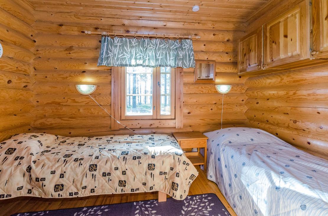 Hirsiseinäinen makuuhuone, jossa kaksi erillistä sänkyä