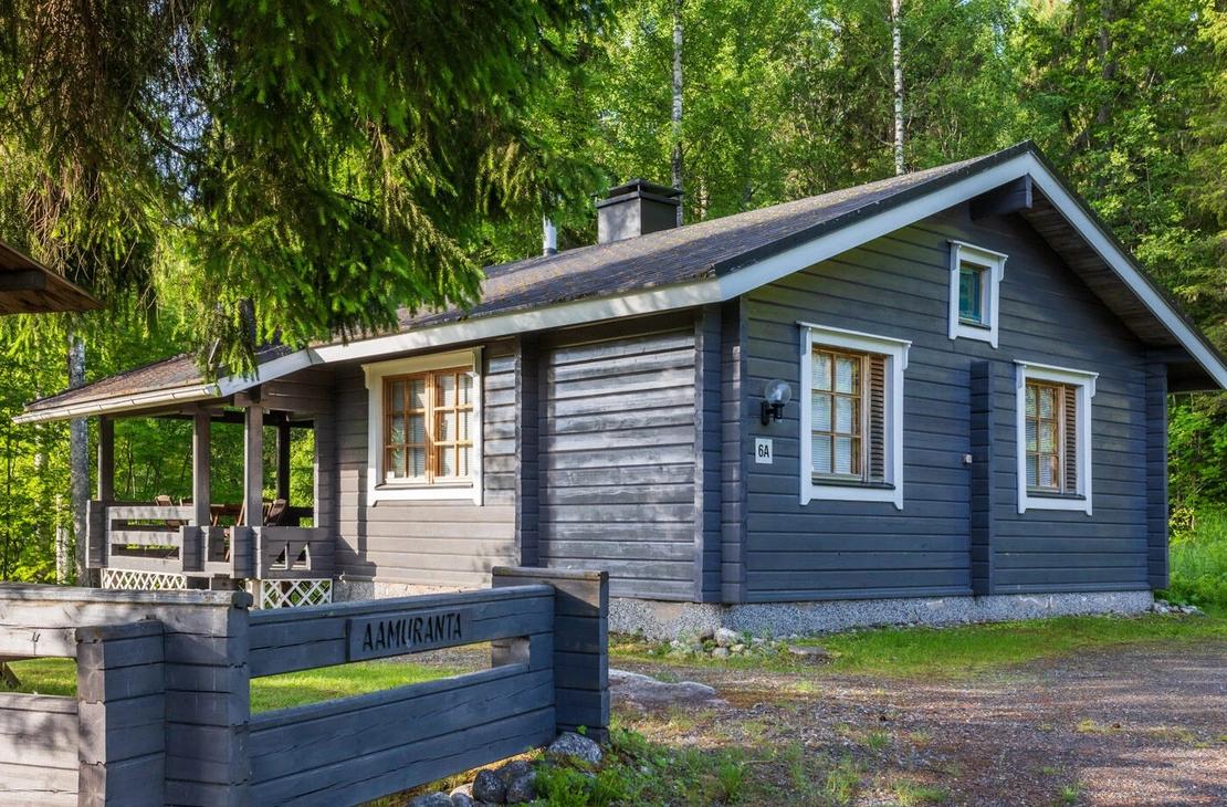 Harmaaksi maalattu h&ouml;yl&auml;hirsinen m&ouml;kkin mets&auml;n reunassa. 