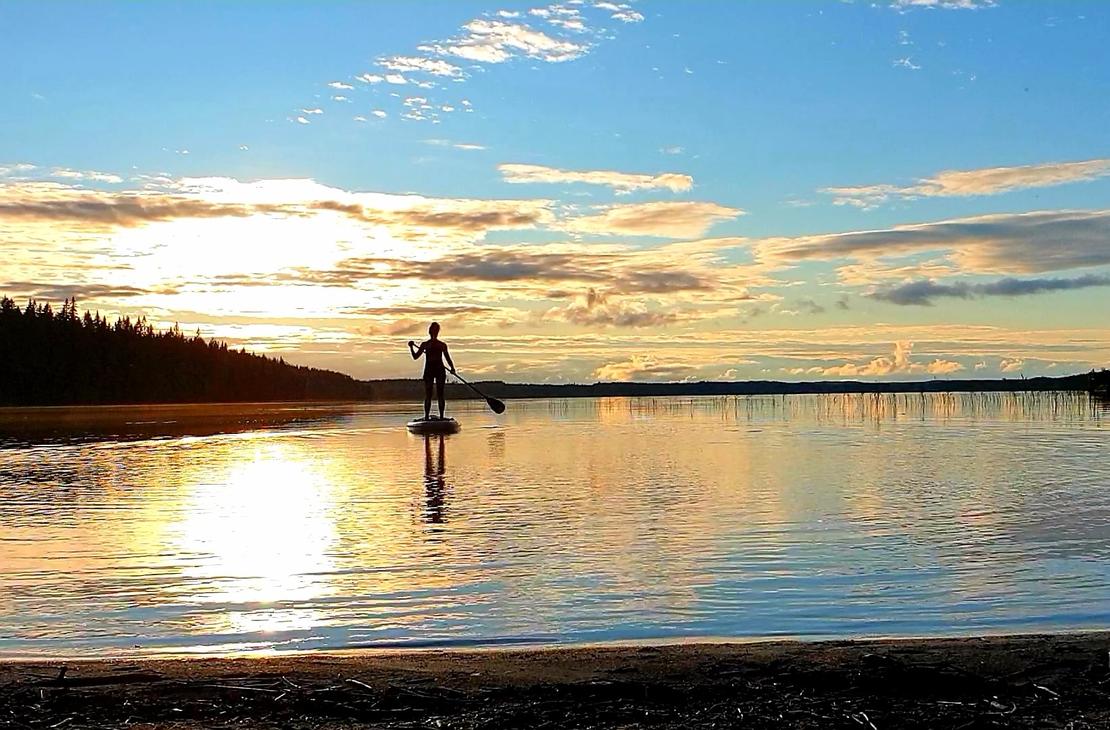 Suppailija tyynell&auml; j&auml;rvell&auml; auringon laskiessa niemen taa