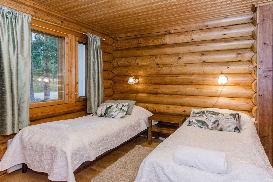 Pyöröhirsiseinäinen makuuhuone, jossa kaksi sänkyä ja vaaleat sänkypeitot