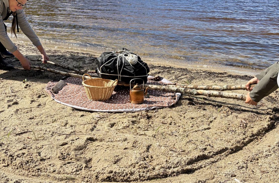 Hiekkarannalla nostetaan raskasta taakkaa keppien avulla