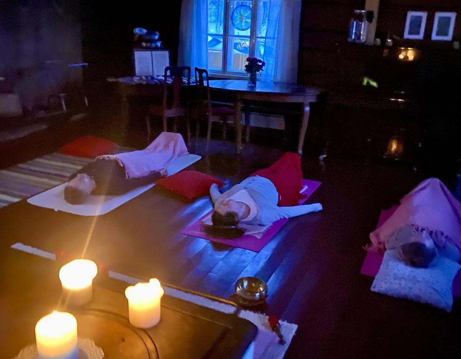 Ihmisiä kuuntelemassa rentoutusta värikkäiden vilttien alla hämärässä kynttilän valossa