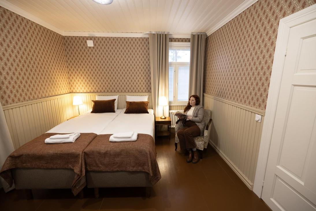 Vaalean ja punaruskean sävyinen huone, jossa kaksi sänkyä ja puiset vaaleat puolipaneelit.