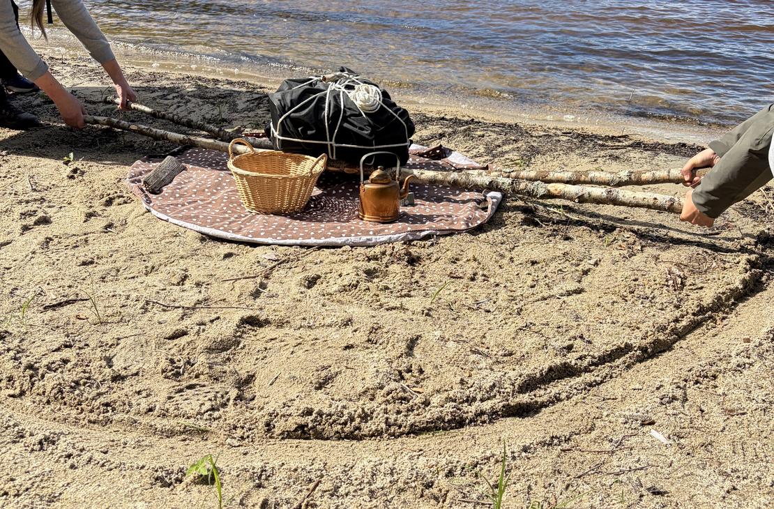 Hiekkarannalla nostetaan raskasta taakkaa keppien avulla