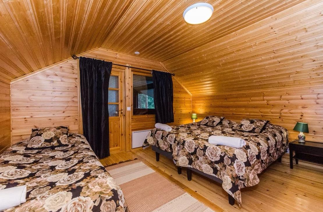 Yläkerran makuuhuone, jossa kalteva katto ja värikkäät tummapohjaiset sänkypeitot