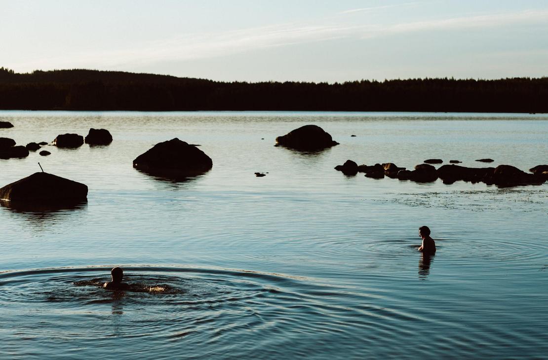 Ihmisiä uimassa tyynellä järvellä illan hämyssä